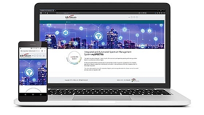 A laptop and smartphone displaying the LS telcom website featuring an integrated and automated spectrum management system with a city skyline background and network icons.